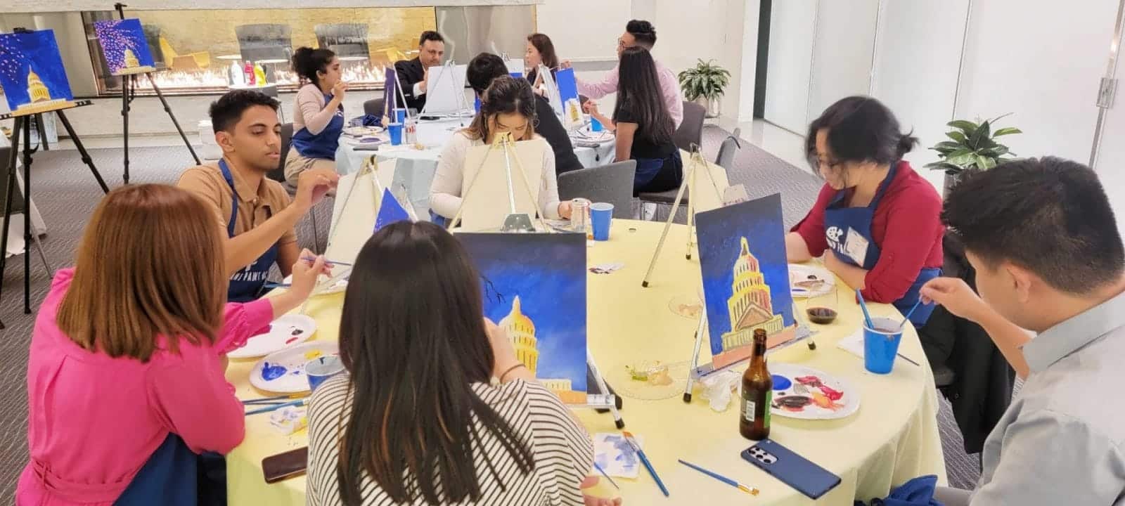 A group of people enjoying a paint and sip session at a table in an office.