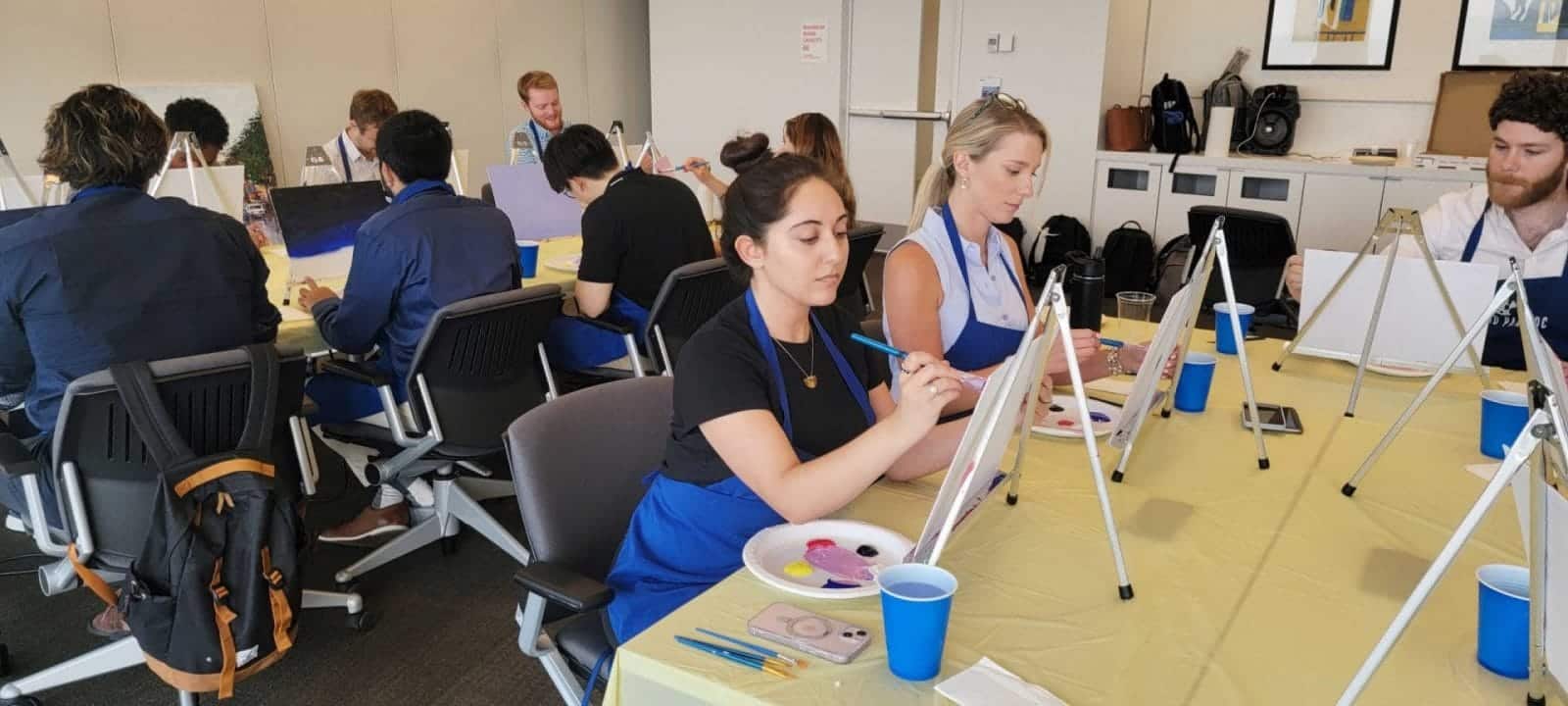 A group of people engaging in a sip and paint activity at an office.