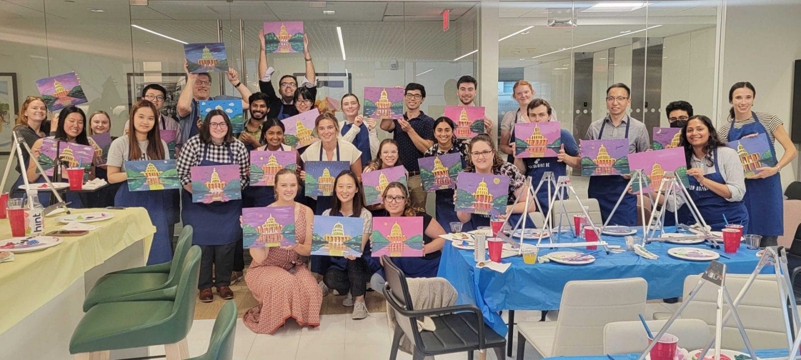 A group of people enjoying a paint and sip while showcasing their artwork in a Washington DC office.