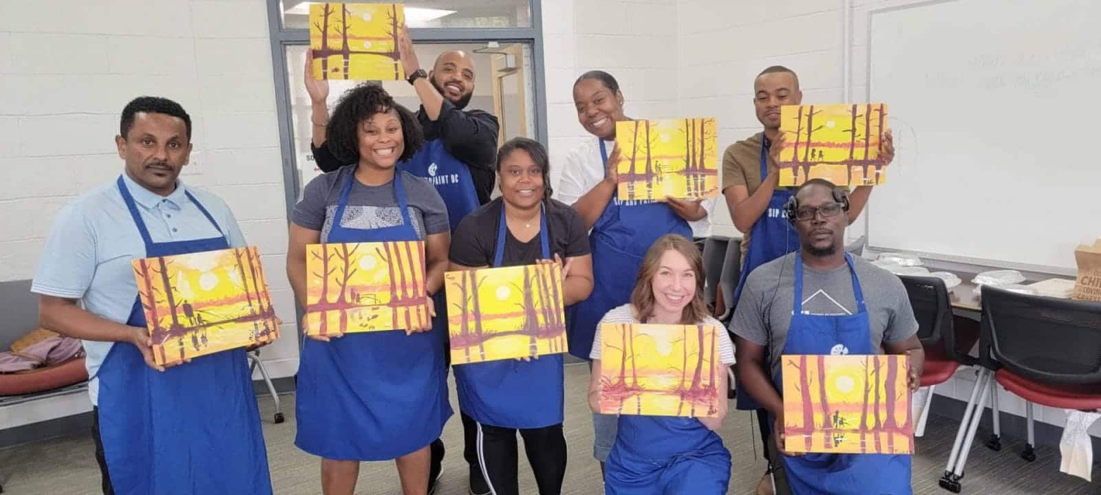 A group of people in a Sip and Paint DC blue aprons participating in a paint and sip session.