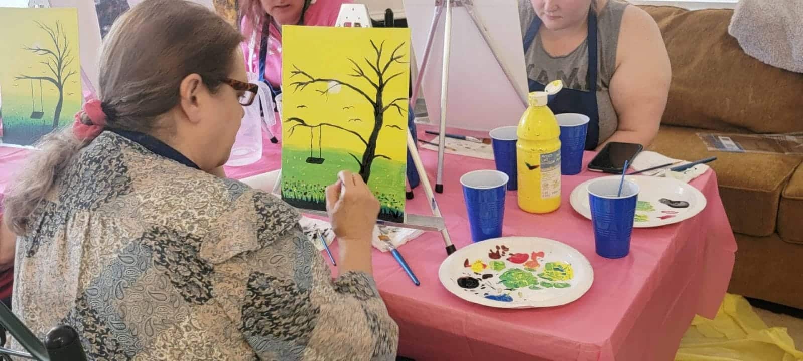 A woman participating in a paint and sip session, creating a masterpiece at a table.